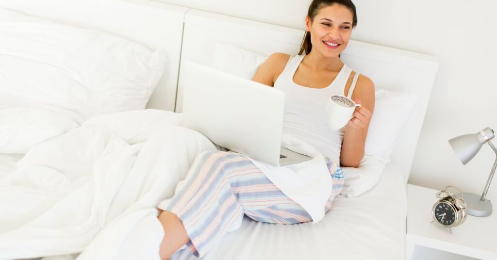 Kvinde sidder med bærbar og kaffe i sengen